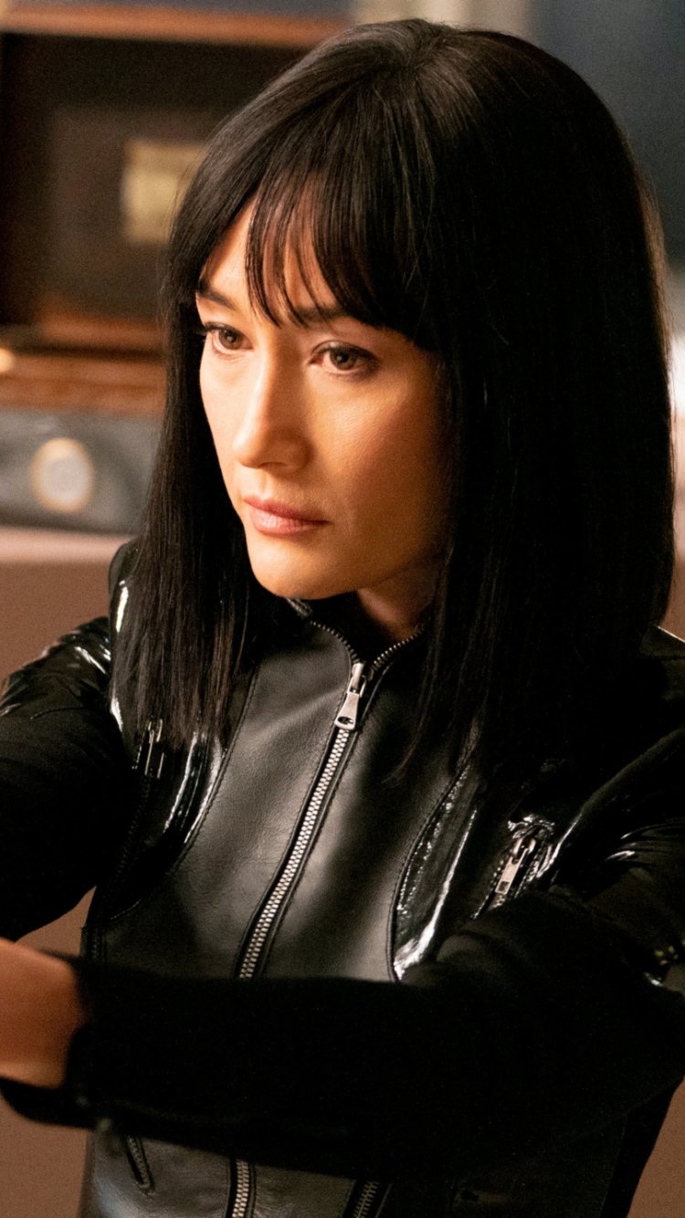 Phone wallpaper featuring Maggie Q as a character from the movie The Protégé, designed for display on iPhones and Android devices.
