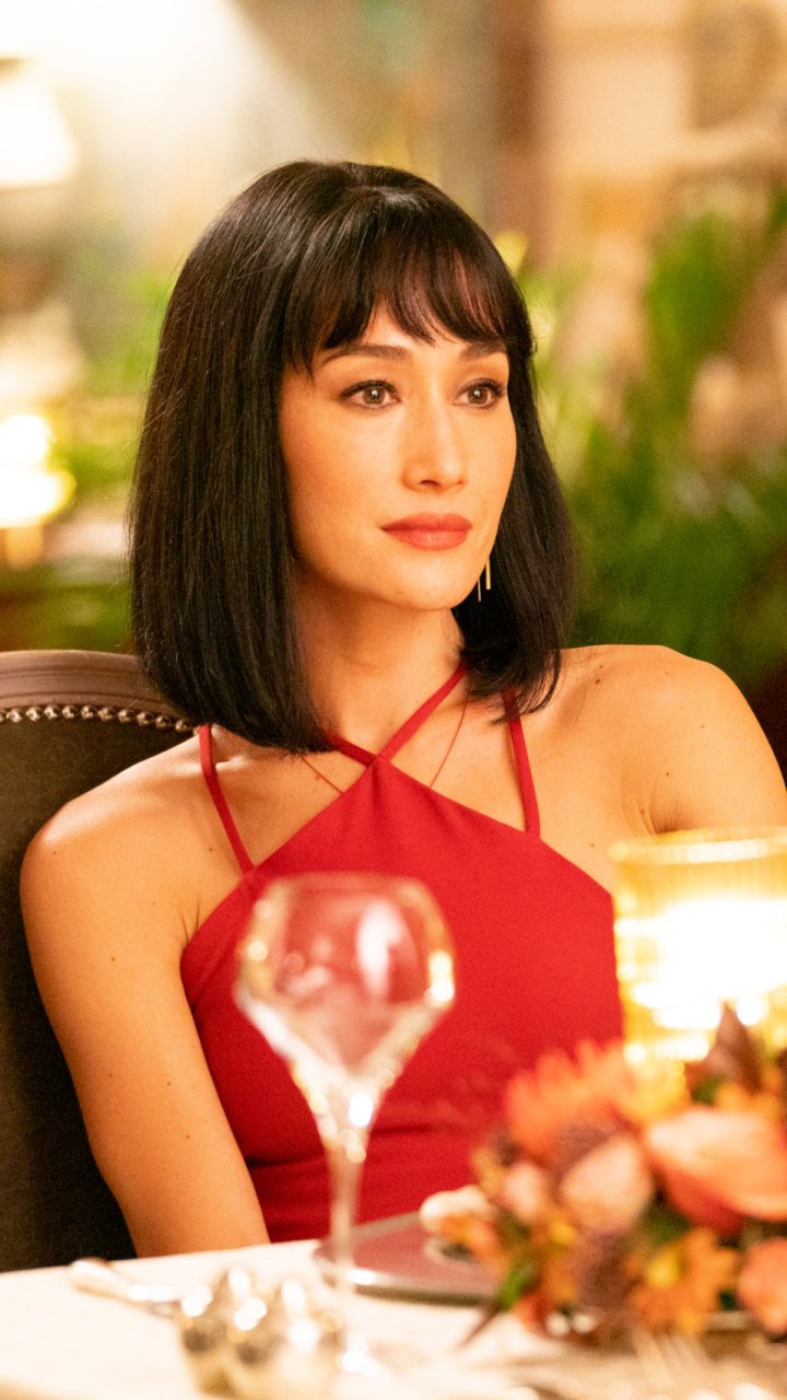 Phone wallpaper featuring Maggie Q from the movie The Protégé, showcasing her in a red dress with a softly blurred warm background.