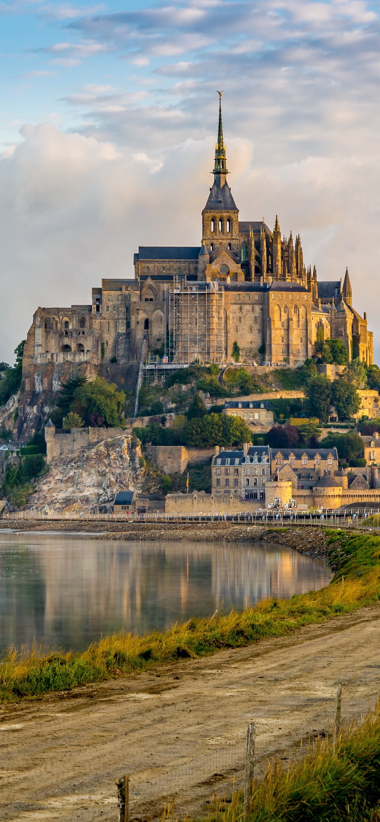 Phone wallpaper: Mont Saint-Michel, Normandy — medieval abbey and religious architecture on a tidal island in France, bathed in golden light and reflected in calm water.