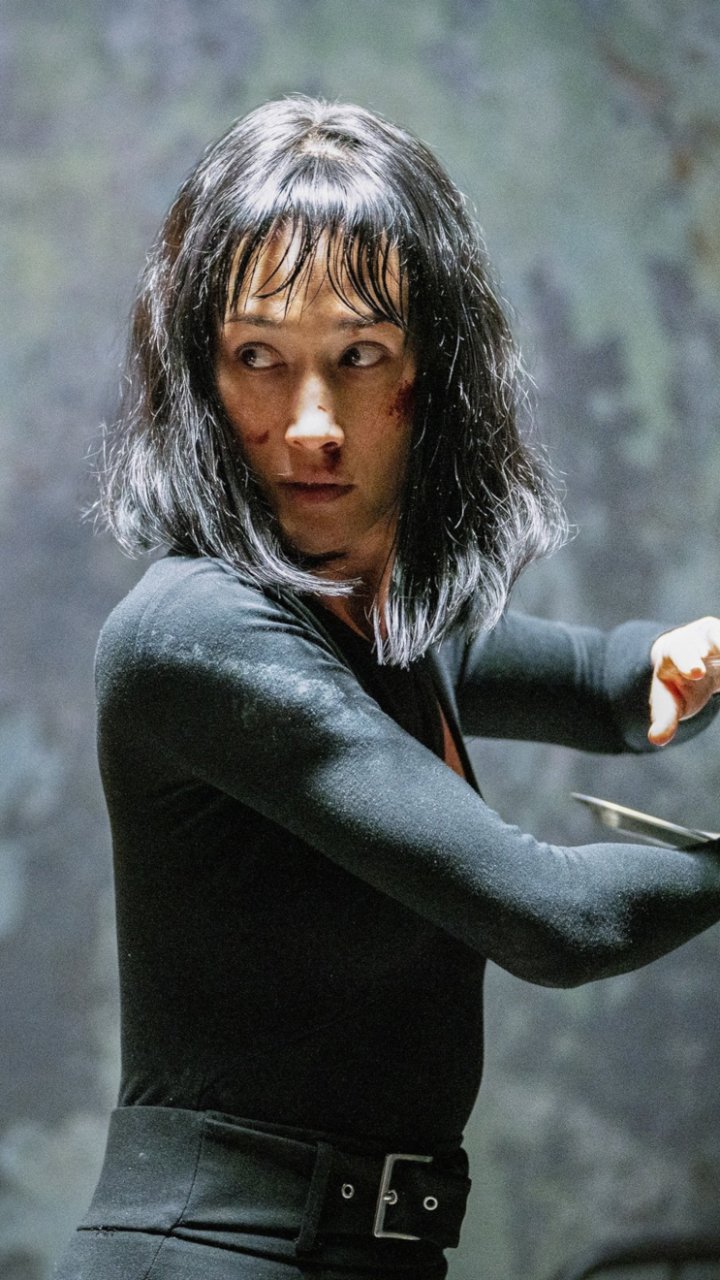 Phone wallpaper featuring Maggie Q as a poised action character from the movie The Protégé, designed for iPhone and Android displays.