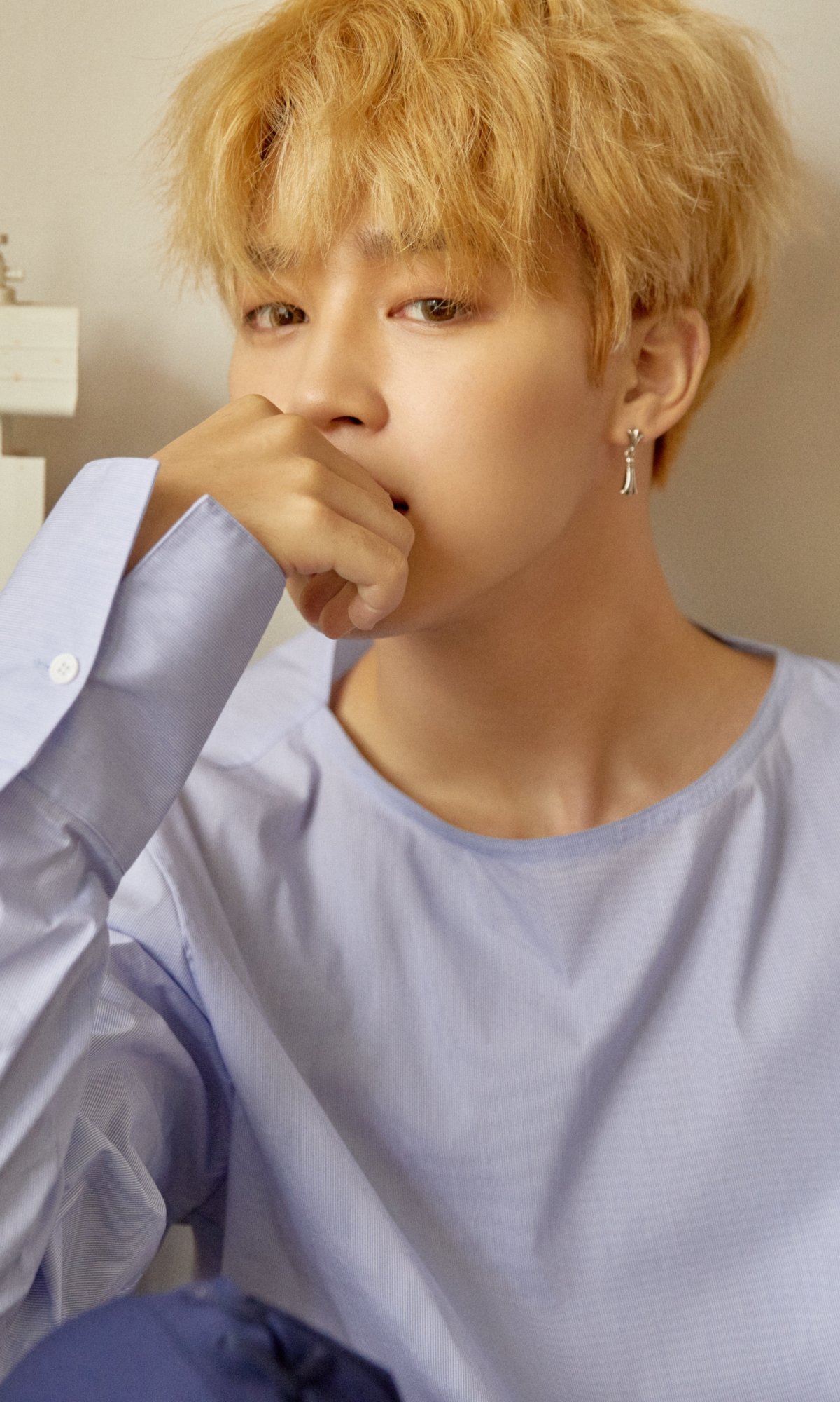 Phone wallpaper of a blond K-pop singer in a pale blue shirt, contemplative pose conveying contemporary K-pop music and fan aesthetic.