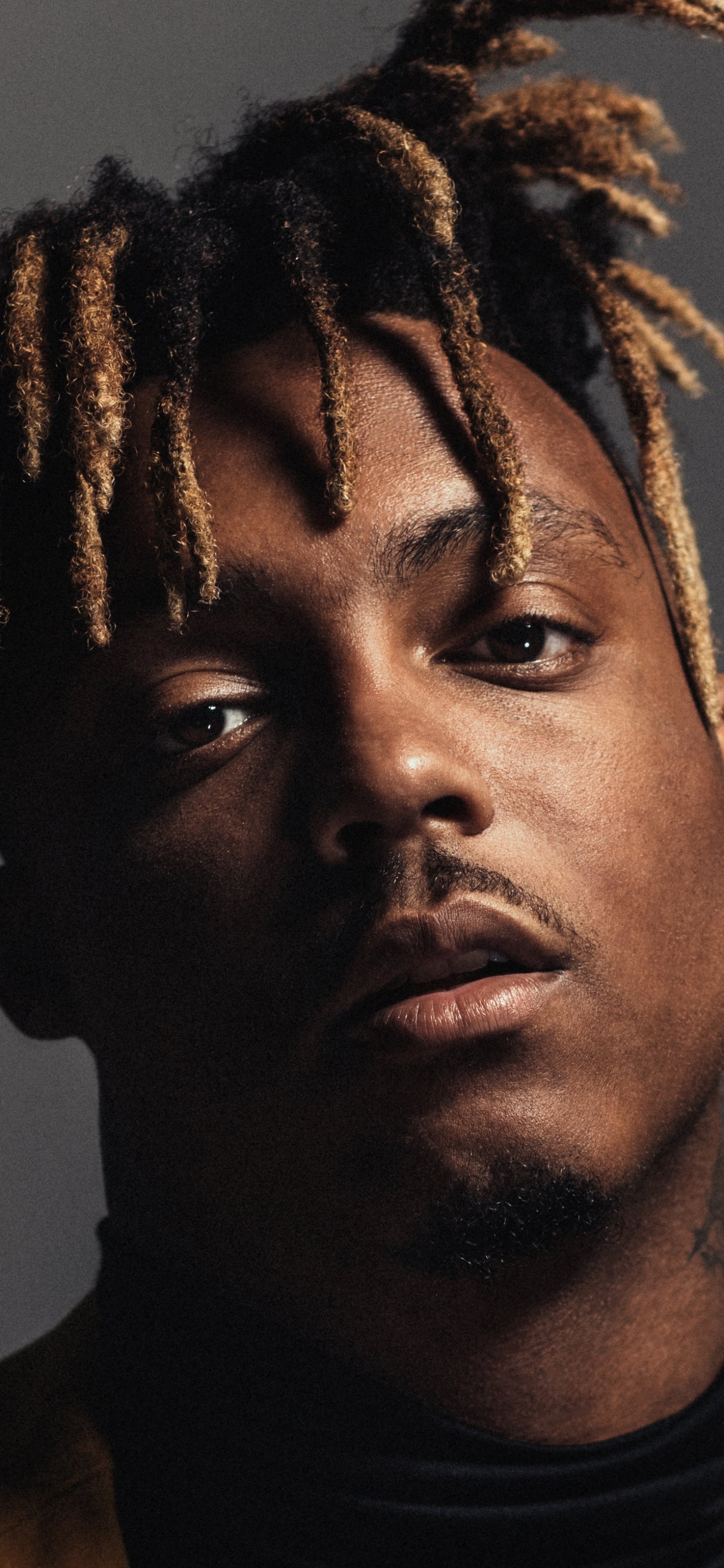 Close-up portrait of a male rapper/singer with blond-tipped dreadlocks, intense gaze and moody lighting, composed vertically as a phone wallpaper.