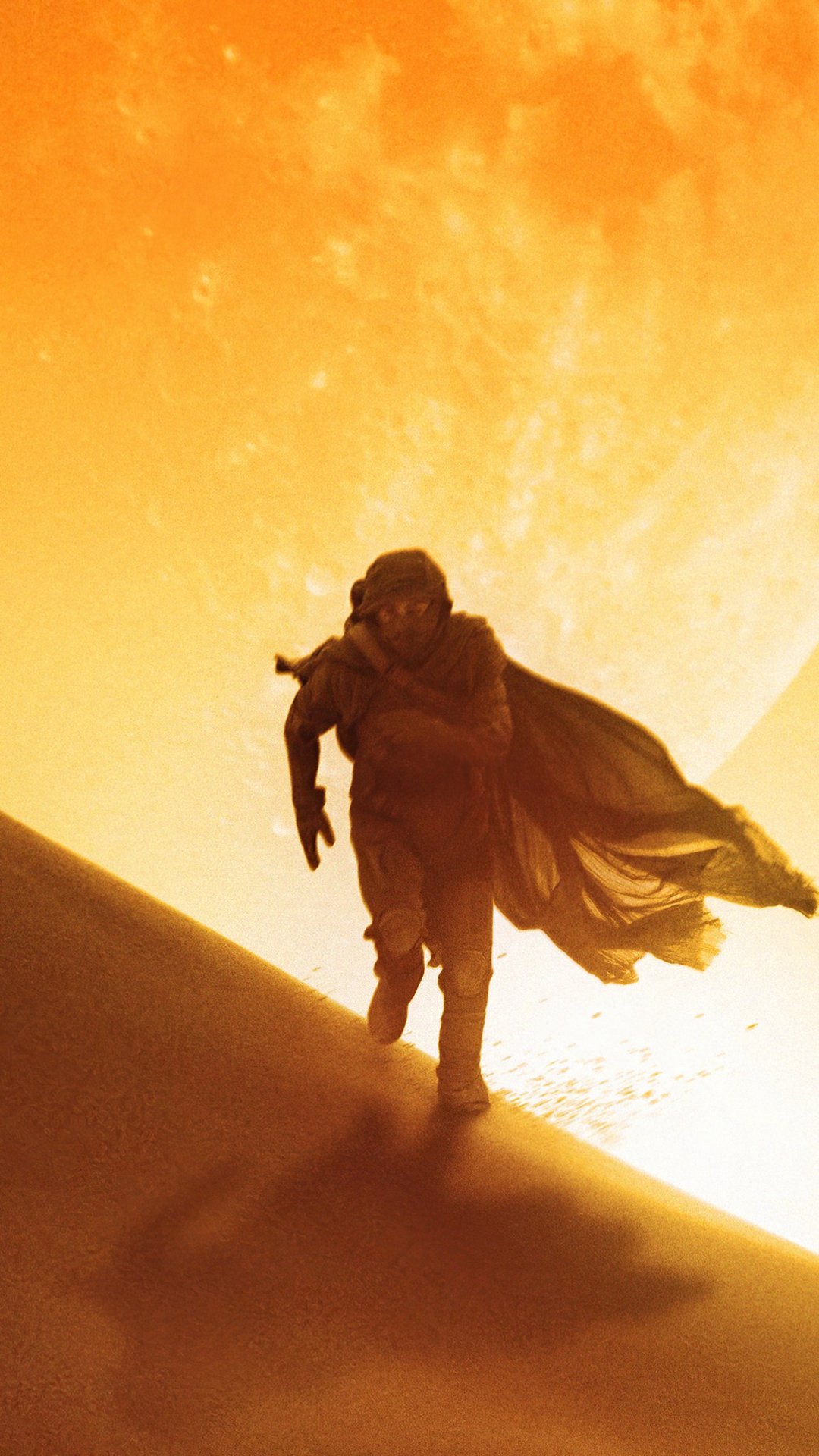Phone wallpaper from Dune (2021): silhouetted figure in a desert cloak walks up a sand dune, backlit by a huge, blazing orange sun.