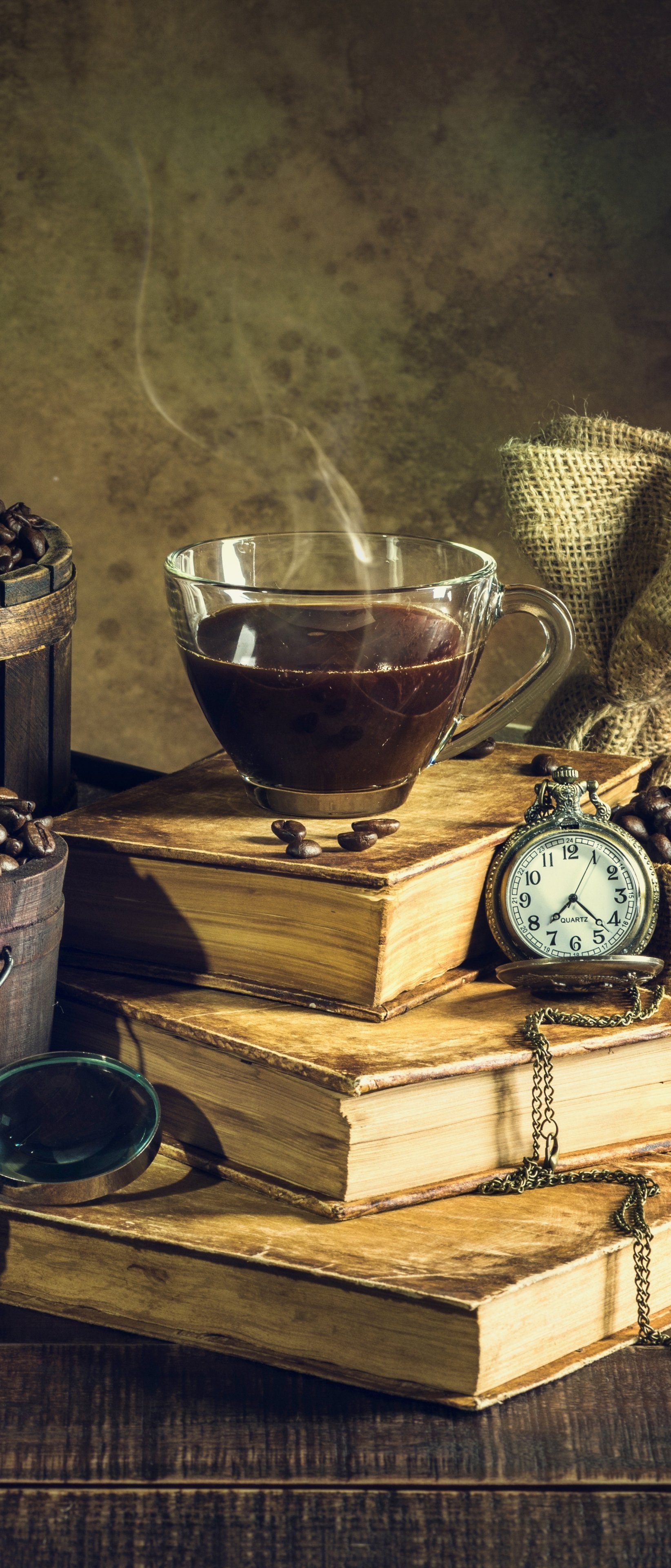 Vertical phone wallpaper: steaming coffee drink atop stacked books with a pocket watch and coffee beans — warm, vintage food-themed still life.
