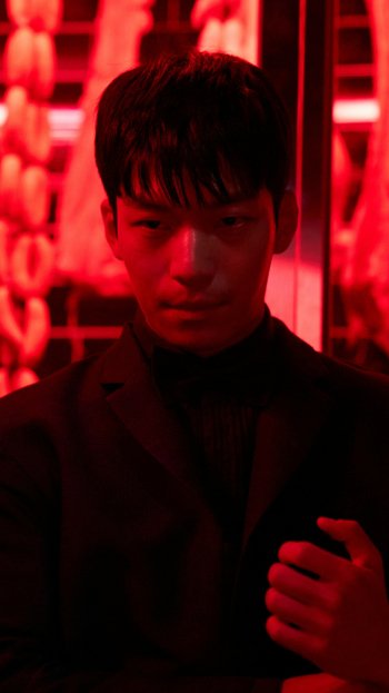 Phone wallpaper featuring Wi Ha-joon as Hwang Jun-ho from the TV show Squid Game, with a striking red background and intense expression, compatible with iPhones and Android devices.