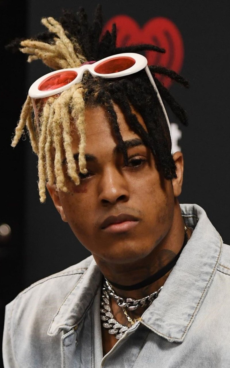 Phone wallpaper featuring a close-up of musician XXXTentacion with distinctive two-tone dreadlocks and white sunglasses, designed for iPhones and Android devices.
