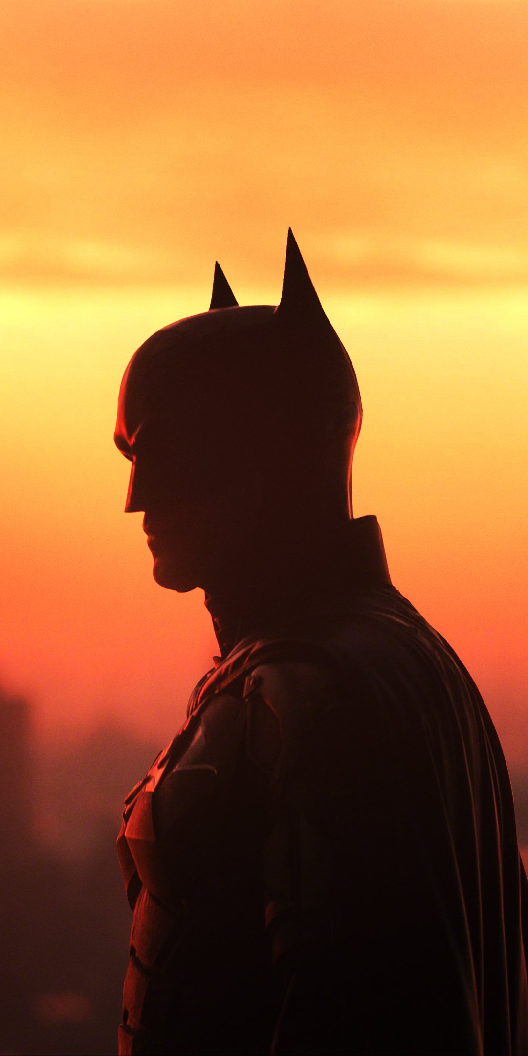 Silhouette of Batman from the movie The Batman against a glowing orange sunset, rendered as a moody phone wallpaper.