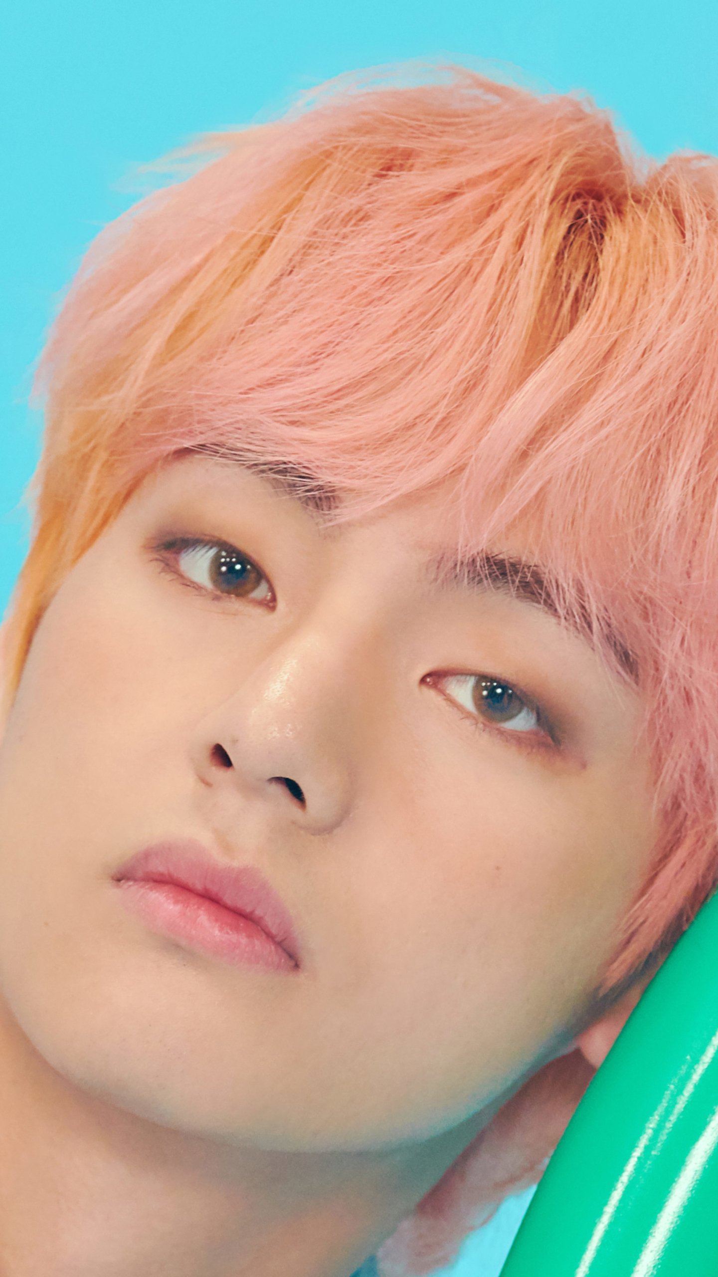 Phone wallpaper close-up of a pink‑haired young person against a turquoise background, soft gaze and subtle makeup, music fan aesthetic.