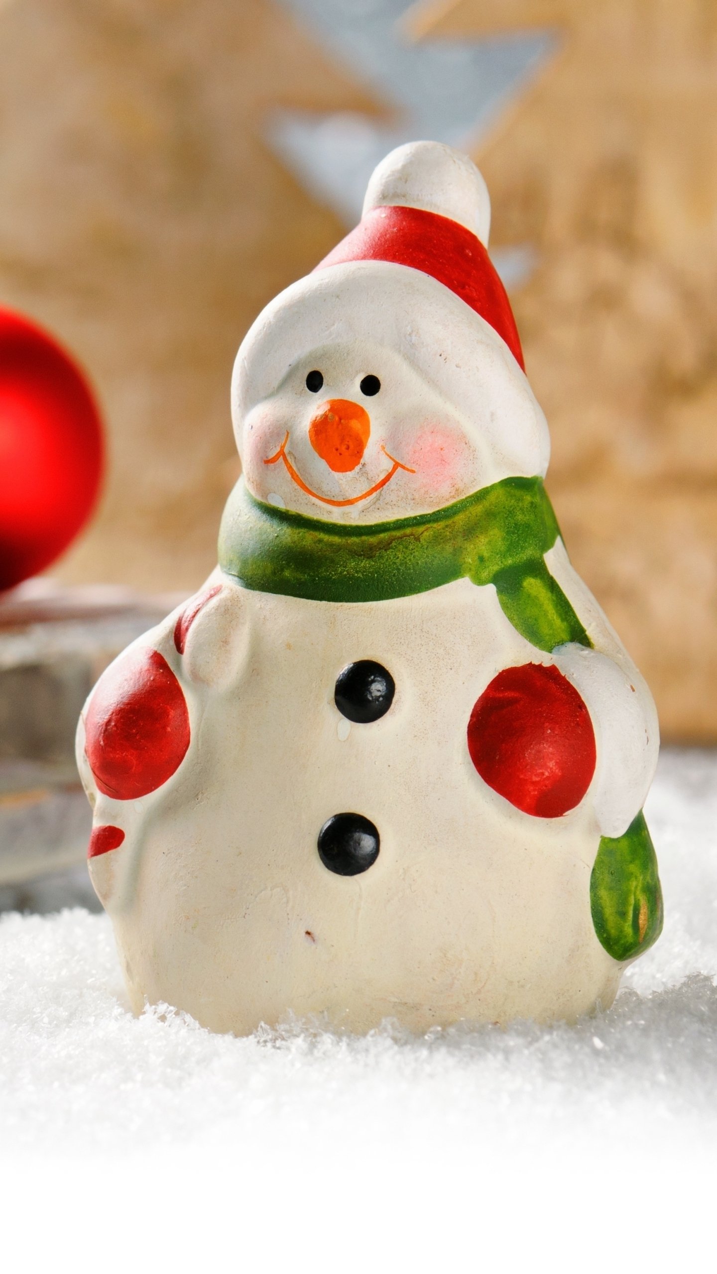 Christmas-themed phone wallpaper featuring a smiling snowman with a red hat and green scarf standing on snow, set against a blurred festive background.