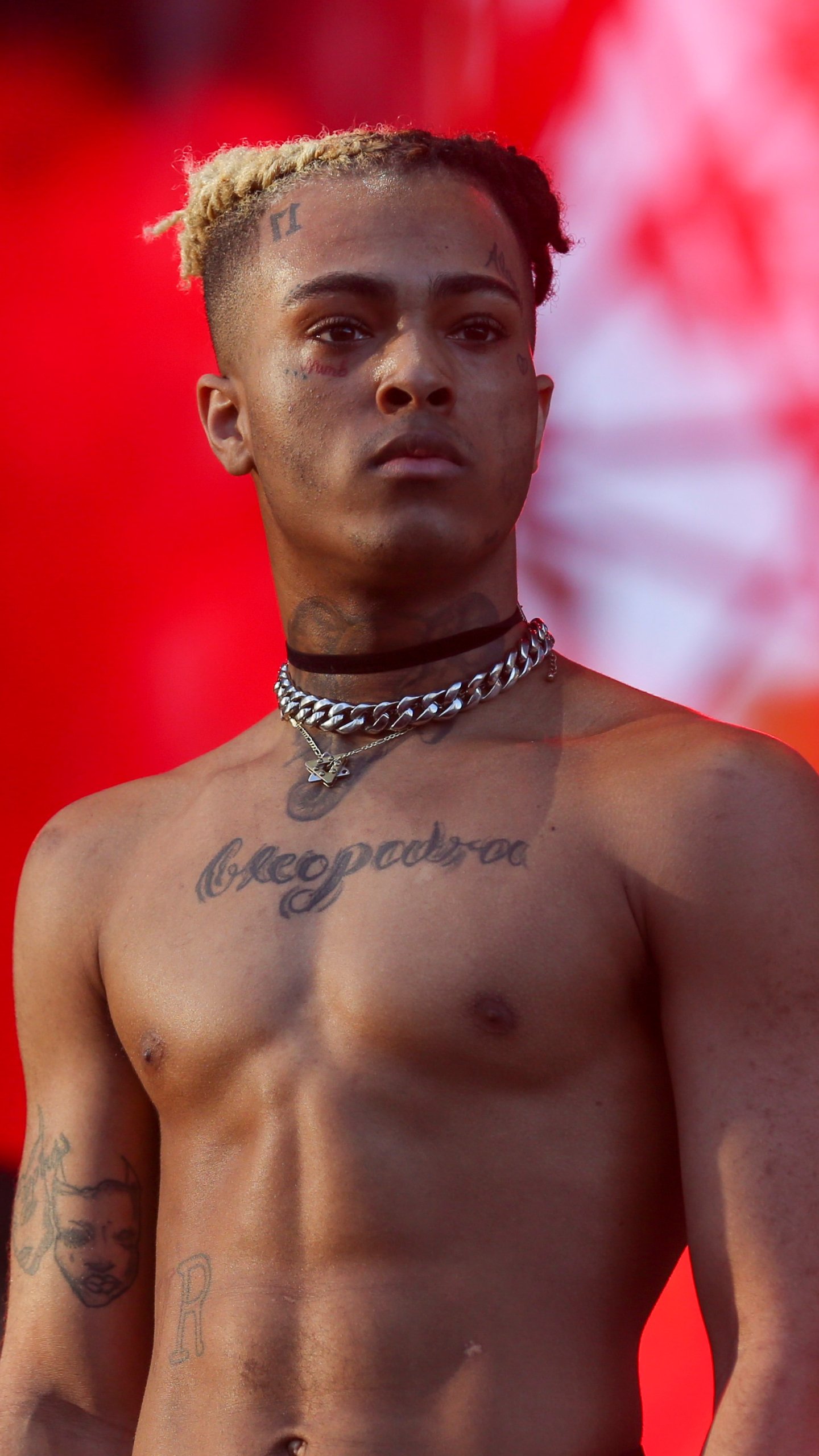 Phone wallpaper featuring a shirtless XXXTentacion against a vibrant red background, designed for both iPhone and Android devices.