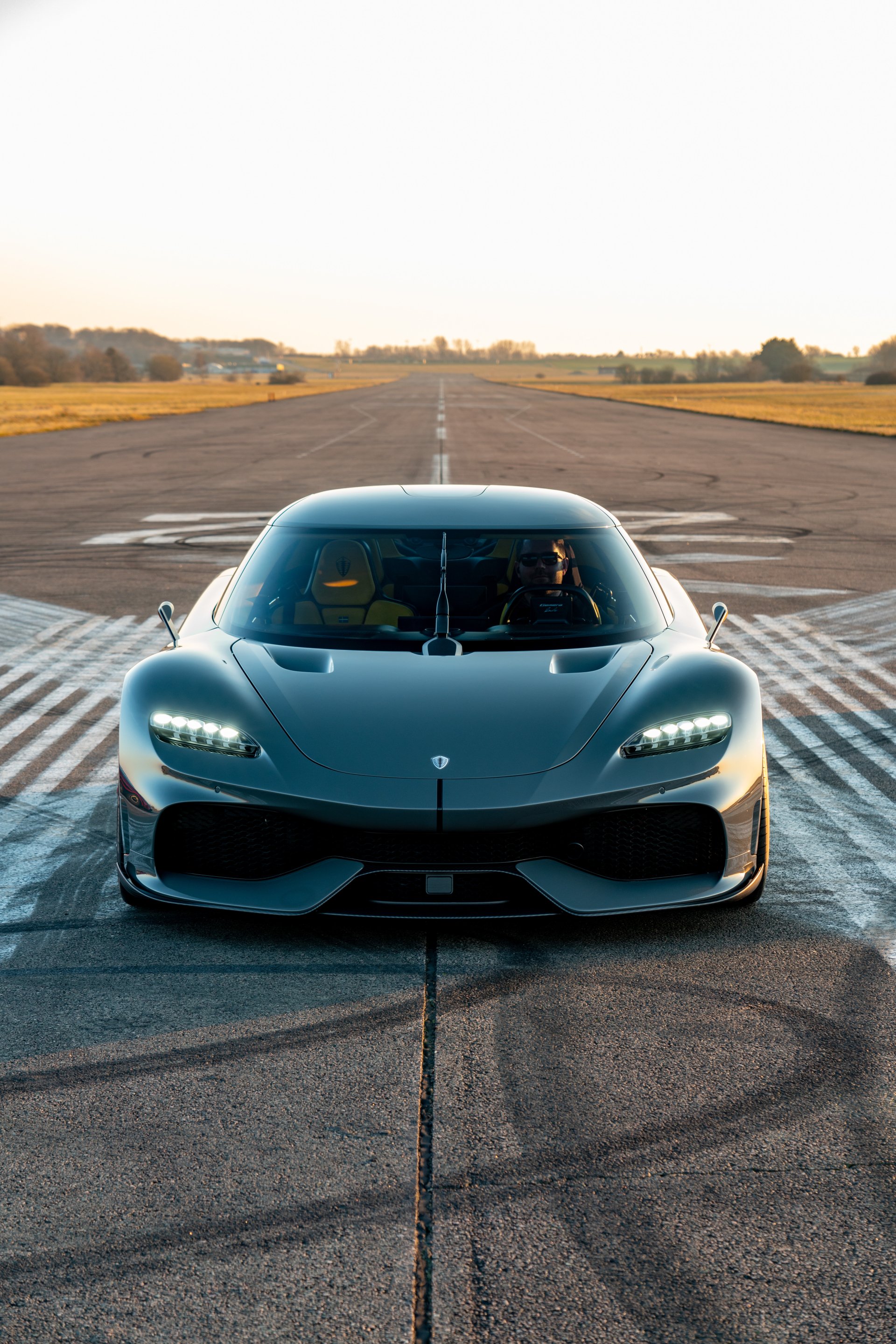 A sleek Koenigsegg Gemera stands poised on an empty runway, showcasing its aerodynamic design and powerful presence, making a striking phone wallpaper for car enthusiasts.