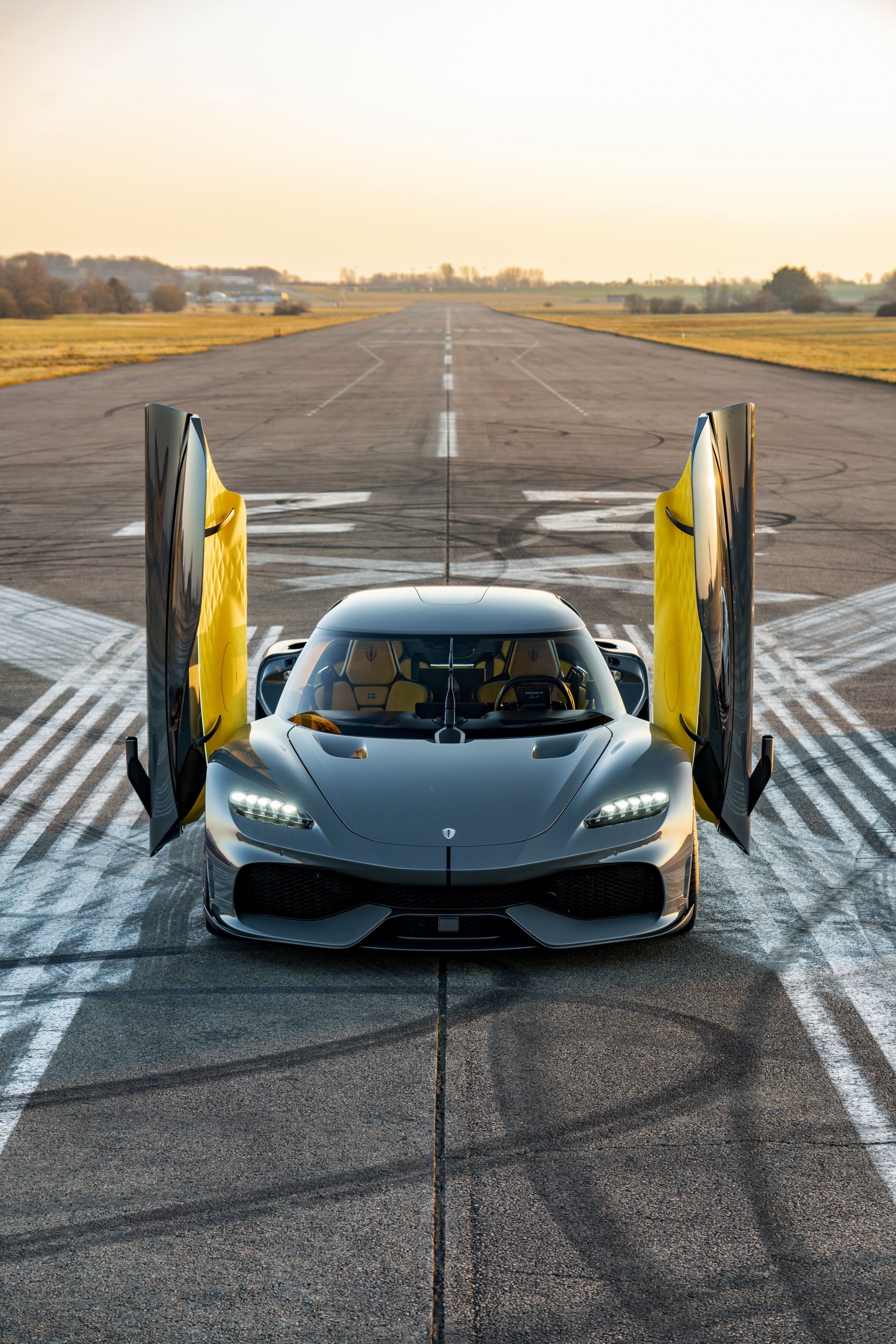 A stunning Koenigsegg Gemera with its doors up, positioned on an empty runway, creating a striking phone wallpaper that showcases its sleek design and incredible engineering.