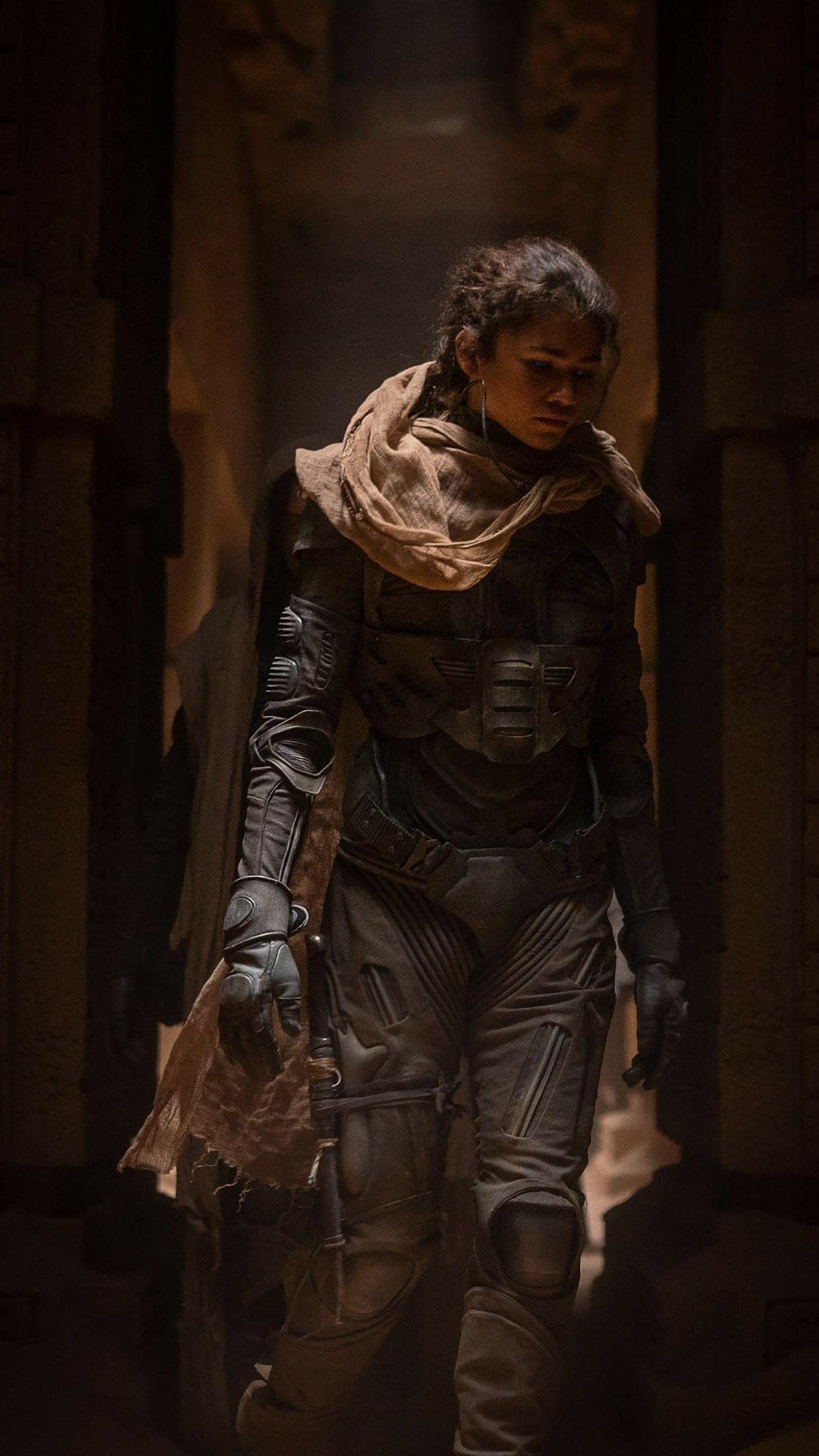 Dune Part Two themed phone wallpaper featuring a character in futuristic desert attire walking through dimly lit, ancient stone corridors.